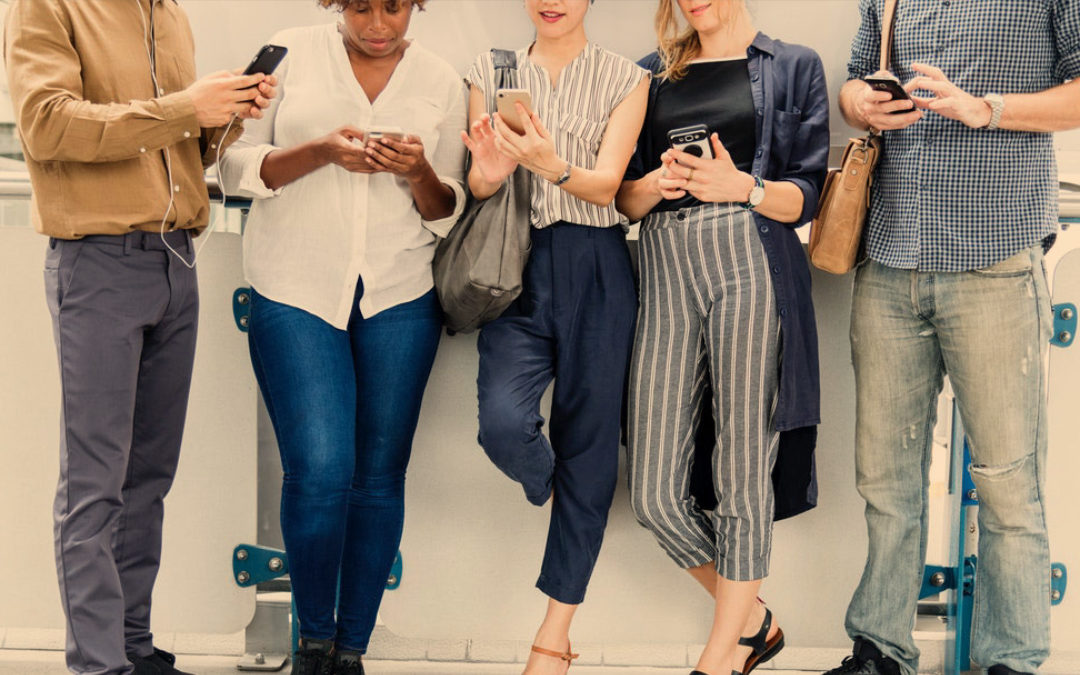 Five people standing up dressed casual texting on smartphones