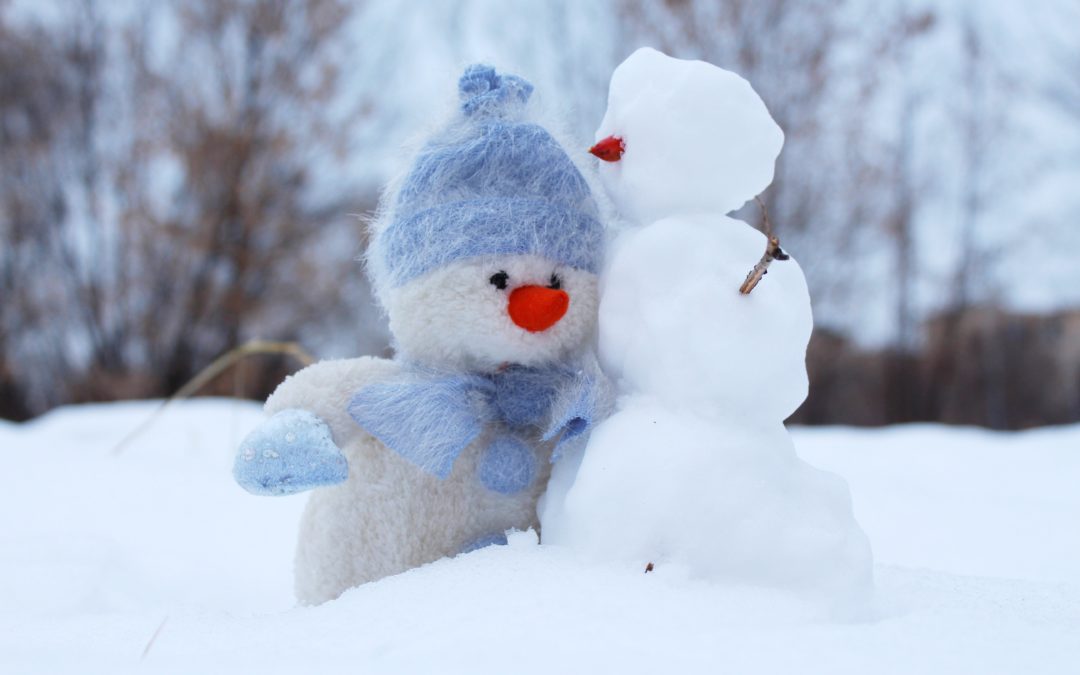Two small snowmen one is dressed in a blue winter hat and scarf.