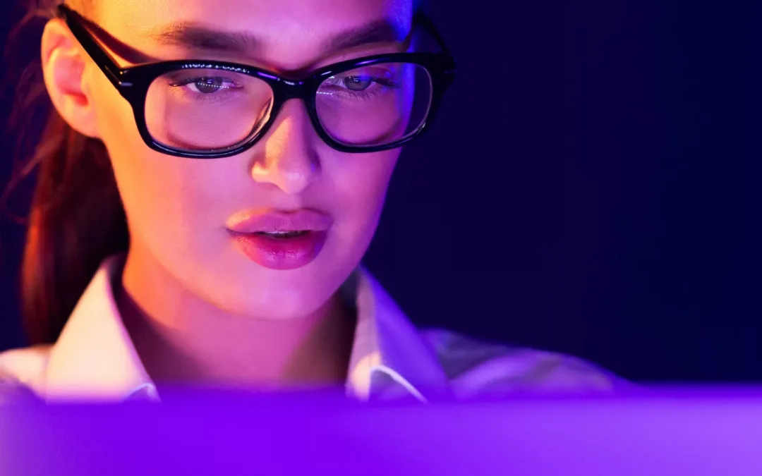 Young woman working on laptop late at night, face illuminated by neon light, free space