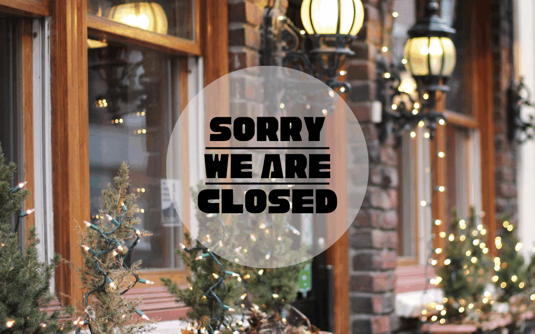 An image of a small business store front that says "Sorry We Are Closed". The image has holiday lights on the bushes outside.